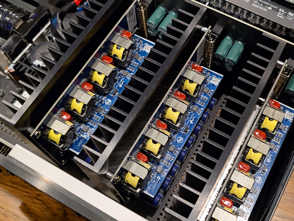 Close-up of an electronic power supply or amplifier chassis showing internal circuit boards with blue PCBs, yellow and red components, and green capacitors.