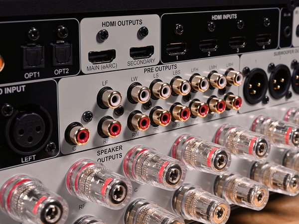 Close-up of the rear panel of an audio receiver or amplifier, showing HDMI outputs, HDMI inputs, optical inputs, speaker outputs, and multiple clear speaker connectors with red rings.