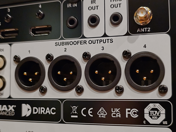 Close-up of the rear panel of a Dirac Advanced subwoofer, showing four XLR subwoofer outputs labeled 1 through 4, along with IR IN, IR OUT, TRK OUT, ANT2, and various certification logos.