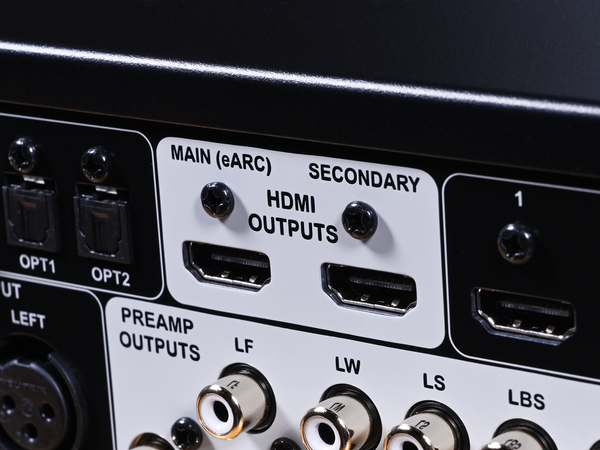 Close-up of the rear panel of an audio device showing HDMI output ports labeled MAIN (eARC) and SECONDARY, along with optical, preamp, and speaker outputs.